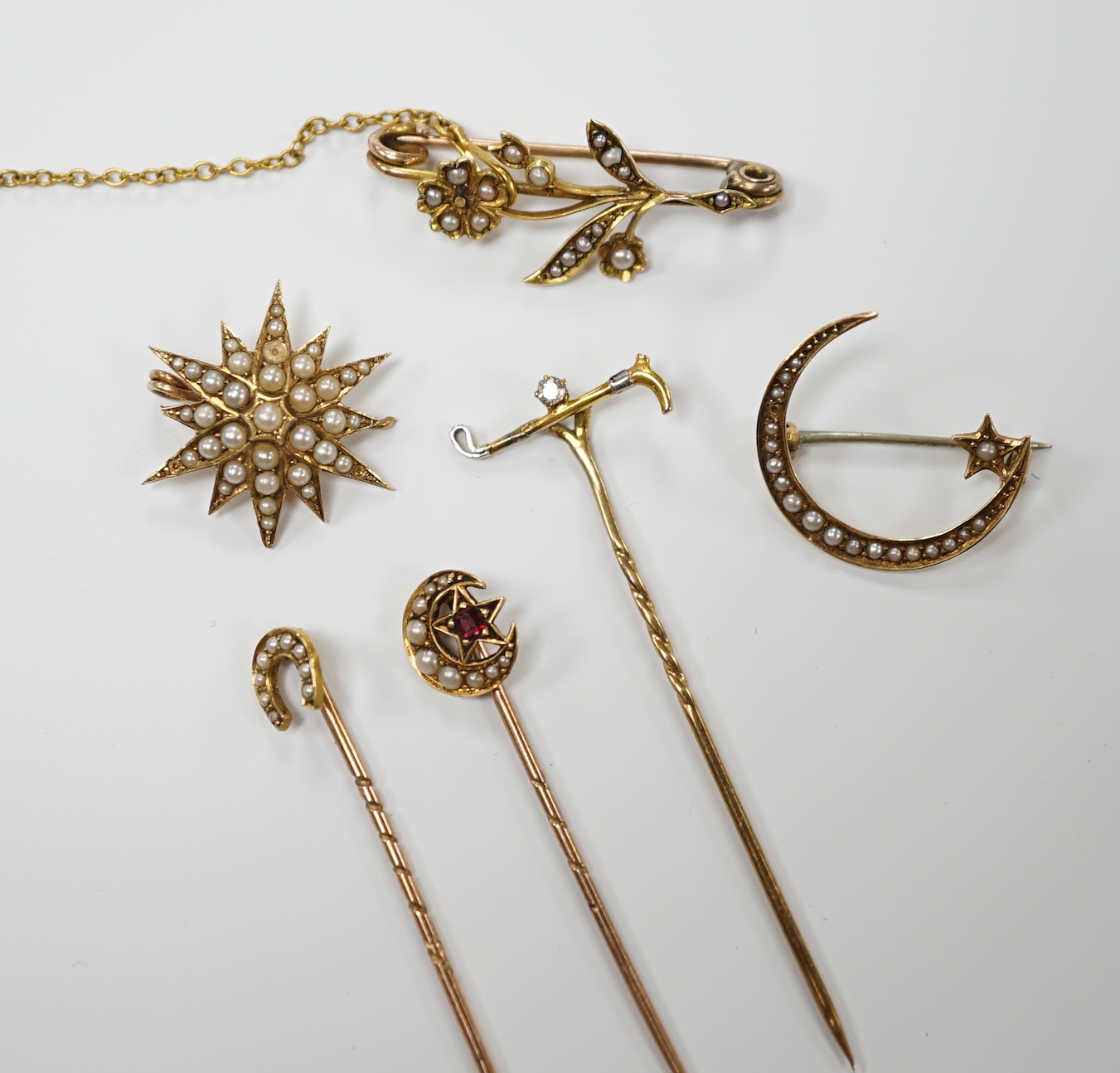 Three early to mid 20th century yellow metal and seed pearl set brooches, largest 34mm, two similar stick pins and a diamond set riding crop stick pin.